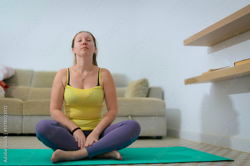 Woman meditating in easy pose on yoga mat in home living room Woman meditating in easy pose on yoga mat in home living room