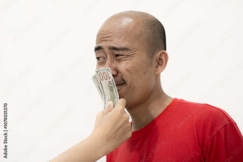 Bald Indonesian man speechless when a wad of dollar bills are slapped in his mouth, isolated on white background. Bald Indonesian man speechless when a wad of dollar bills are slapped in his mouth, isolated on white background.