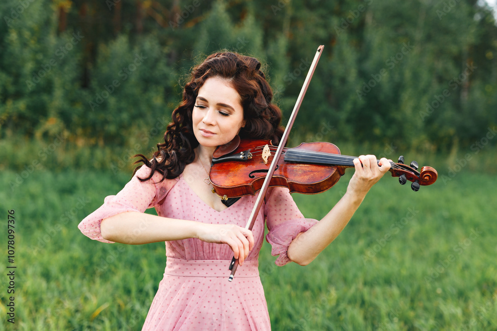 Beautiful girl with curly black hair in pink dress plays the violin in field at summer forest, Beautiful girl with curly black hair in pink dress plays the violin in field at summer forest,