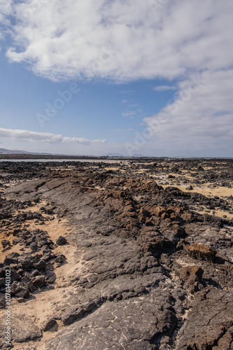 White sand beach with solidified volcanic lava flows, black rocks. Mountains in the background and sky with big white clouds. Caletón Blanco, Lanzarote, Canary Islands, Spain