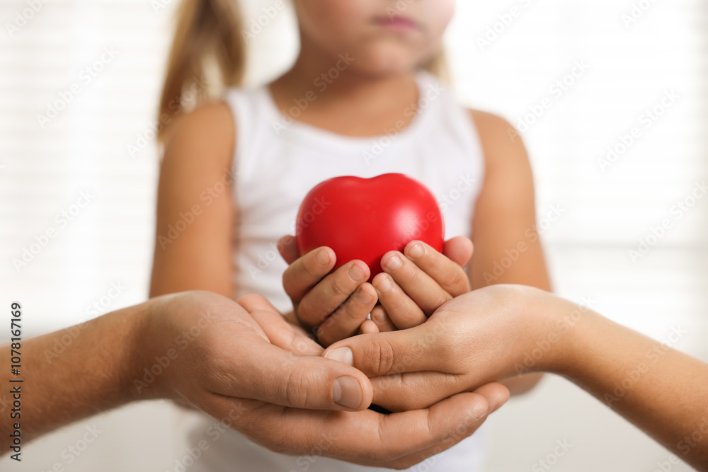Little girl with red heart figure and her parents indoors, closeup Little girl with red heart figure and her parents indoors, closeup
