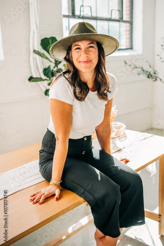 Smiling woman in hat sitting on table in bright, airy room photo