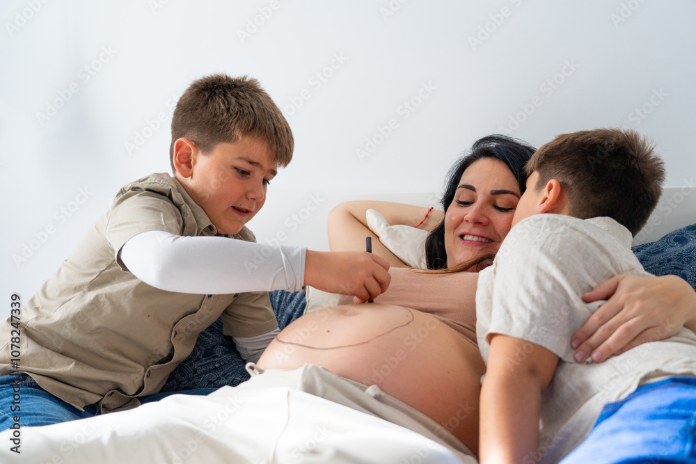 Obraz premium Mother with her two children painting her pregnant belly in the bedroom at home