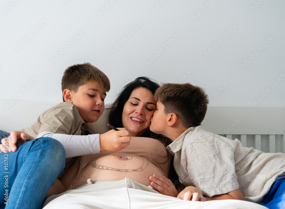 Pregnant woman with her two children at home, one giving her a kiss and the other painting her belly Pregnant woman with her two children at home, one giving her a kiss and the other painting her belly