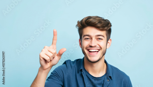 Happy young man pointing finger up with a joyful expression on a light blue