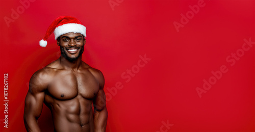 Young black smiling man wearing Santa Claus hat on red background.