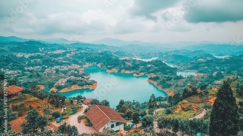 A picturesque view of a lake surrounded by lush green hills, with a few houses nestled into the landscape. The sky is overcast with clouds, adding to the serene atmosphere.