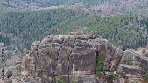 Hikers reach a scenic mountain summit with a striking red flag in the remote wilderness of Siberia during early spring