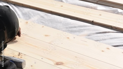 A person hammering a nail into a light wooden plank, demonstrating the construction process within the concept of building a wooden frame house