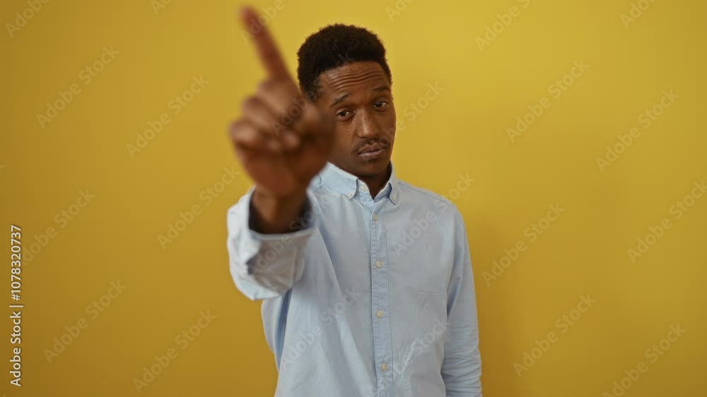 Young african american man wearing shirt standing with finger pointing up in no gesture, showing strong expression over isolated yellow background