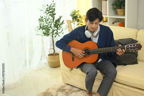 Young man relaxing on sofa and playing guitar in natural light photo