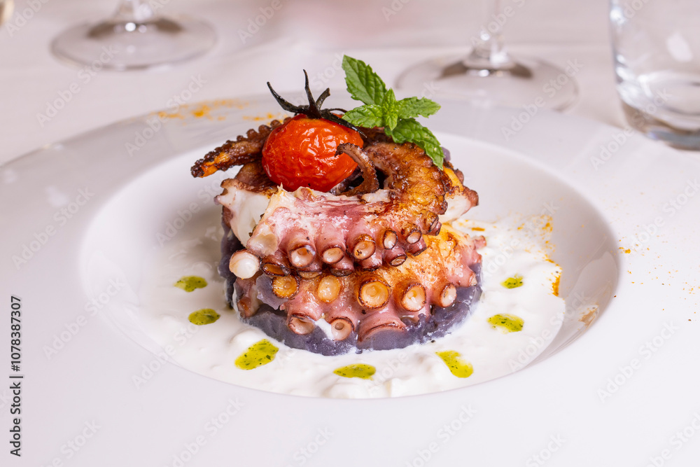 Polpo cotto alla brace e servito su una crema al latte con gocce di pesto di basilico in un ristorante elegante Polpo cotto alla brace e servito su una crema al latte con gocce di pesto di basilico in un ristorante elegante