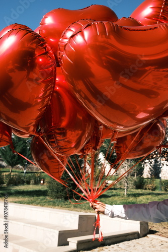 A hand holding bright red heart-shaped balloons in sunlight