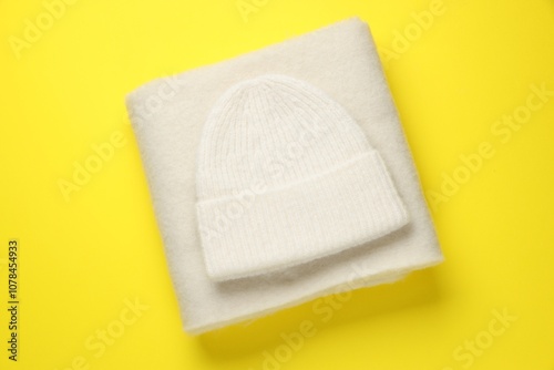 Warm woolen hat and scarf on yellow background, top view