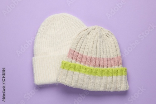 Warm woolen hats on lilac background, top view