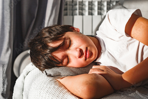 Cute tired boy sleeping in comfortable  sofa in beams of morning sun