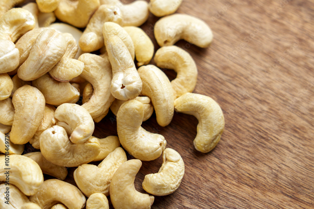 Cashews scattered on a wooden table with creamy color and smooth texture, ideal for a healthy snack or recipe ingredient. Cashews scattered on a wooden table with creamy color and smooth texture, ideal for a healthy snack or recipe ingredient.
