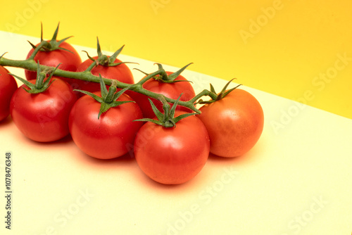 Red cherry tomatoes with green branch on yellow background	 photo