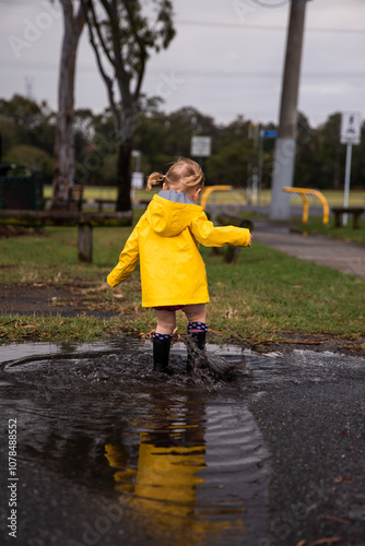 little girl stomping in a puddle wearing bright yellow raincoat photo