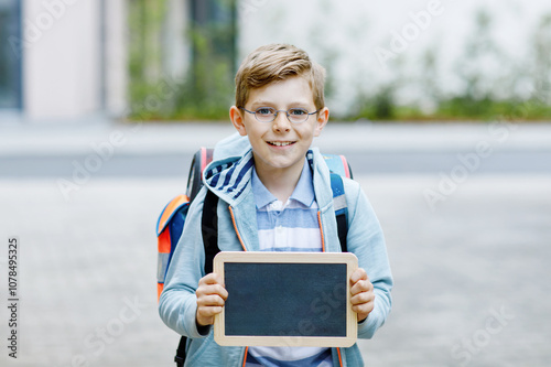 Happy little kid boy with backpack or satchel and glasses. Schoolkid on the way to school. Healthy adorable child outdoors On desk Last day third grade in German. School's out photo