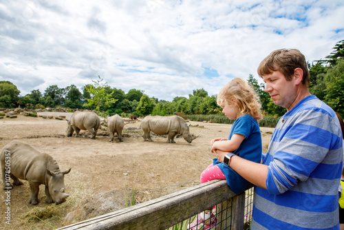 Photography Cute adorable toddler girl and father watching wild rhinos in zoo