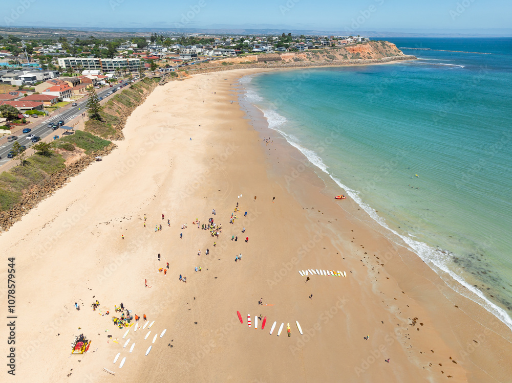 Aerial view of surfboards and beachgoers spread out on a wide sandy beach below a coastal city Aerial view of surfboards and beachgoers spread out on a wide sandy beach below a coastal city