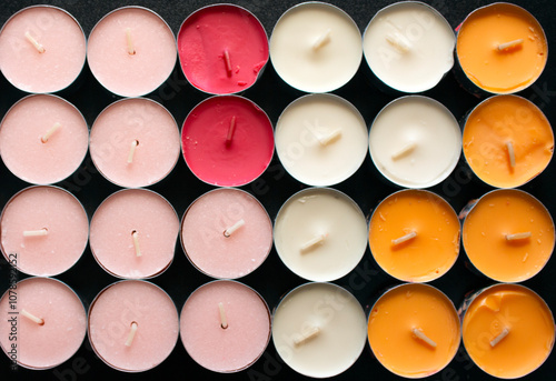 Top view of a group of unused colored Tea Candles on a black table