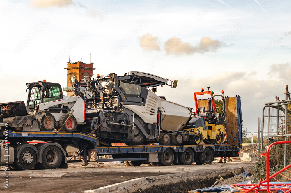 Construction vehicles loaded on a trailer at a construction site during the afternoon in an urban area Construction vehicles loaded on a trailer at a construction site during the afternoon in an urban area
