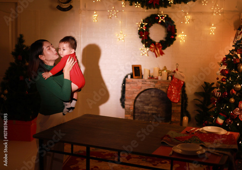 A mother is holding her son and kissing him in a room near the Christmas tree.