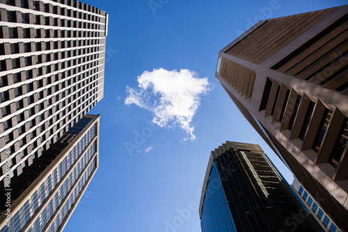 looking up at a single cloud in an otherwise blue sky surrounded by tall city buildings photo