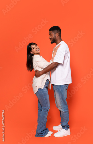 A joyful couple shares an affectionate moment against a bright orange background while embracing each other