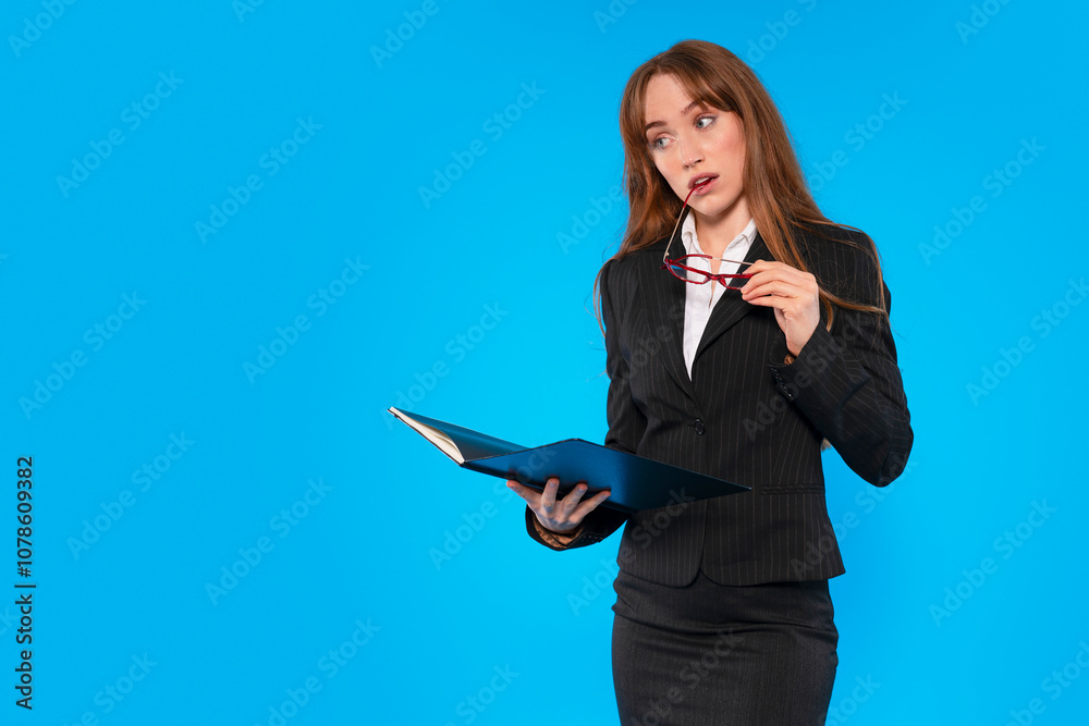 Businesswoman with glasses analyzes report while standing against vibrant blue background in office setting Businesswoman with glasses analyzes report while standing against vibrant blue background in office setting