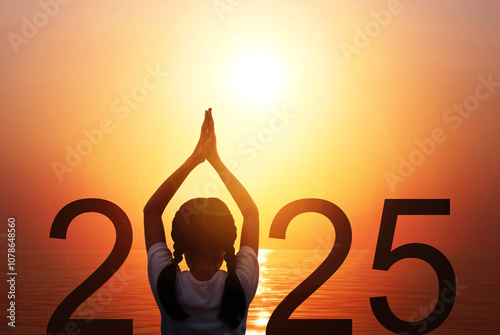 Happy new year 2025. Silhouette of girl doing Yoga vrikshasana tree pose on tropical sea with fantastic sunrise sky background. Back of kid standing as part of Number 2025 sign and watching sunset. photo