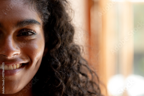 Smiling woman with curly hair basking in warm sunlight through window, copy space, at home photo