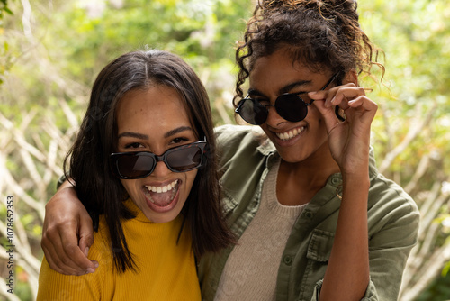 Two multiracial female friends on deck laughing and enjoying sunny day with sunglasses photo