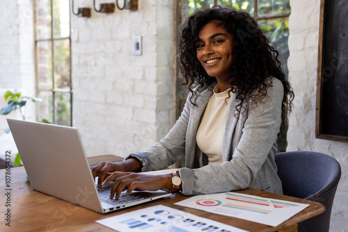 Smiling woman working on laptop at home office with charts on desk photo