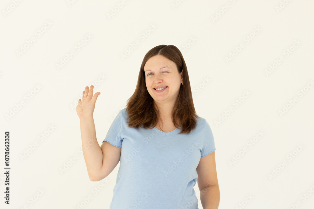 Cheerful friendly girl saying hello, winking and smiling, waving hand at camera, say hi and greet you, standing against white background Cheerful friendly girl saying hello, winking and smiling, waving hand at camera, say hi and greet you, standing against white background