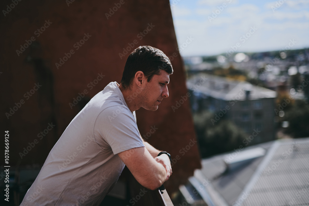 Fototapeta premium A thoughtful man stands on the balcony of a high-rise building and looks at the city panorama