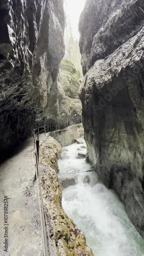 A river stream flows calmly at the base of the rocky valley in Partnach Gorge, Garmisch-Partenkirchen, Germany. Surrounded by towering cliffs and rugged terrain. photo