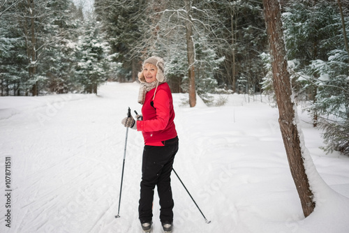 senior active woman outdoots portrarit - skiing in forest. Standing on the snow, looking at camera