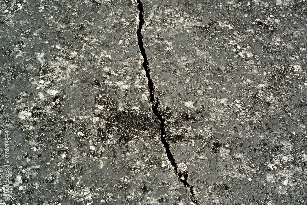 Obraz premium A close-up of a large crack in a gray asphalt surface.