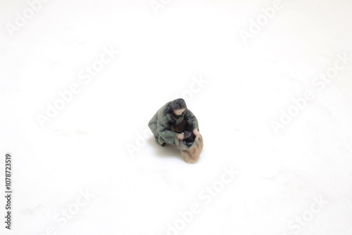 Miniature Figure Of A Person Sitting With Bag On White Surface