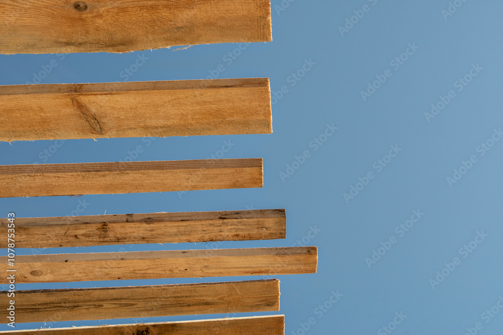 View from below of wooden roof sheathing beams of a frame house against clear sky View from below of wooden roof sheathing beams of a frame house against clear sky