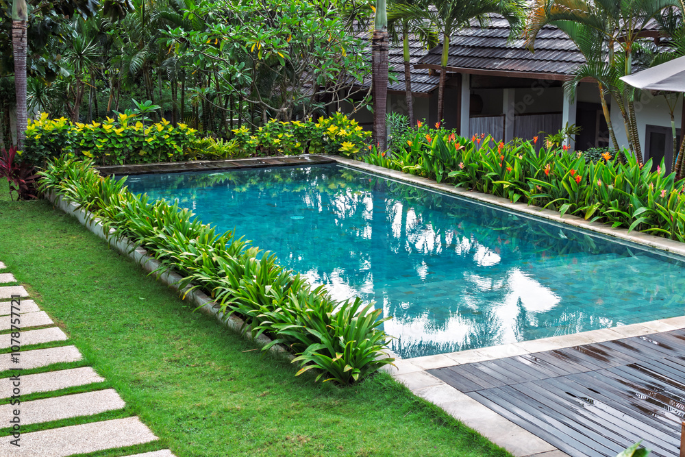 Obraz premium A bright swimming pool with crystal-clear water, surrounded by lush greenery, tropical plants, and pathways, creating a paradise-like atmosphere