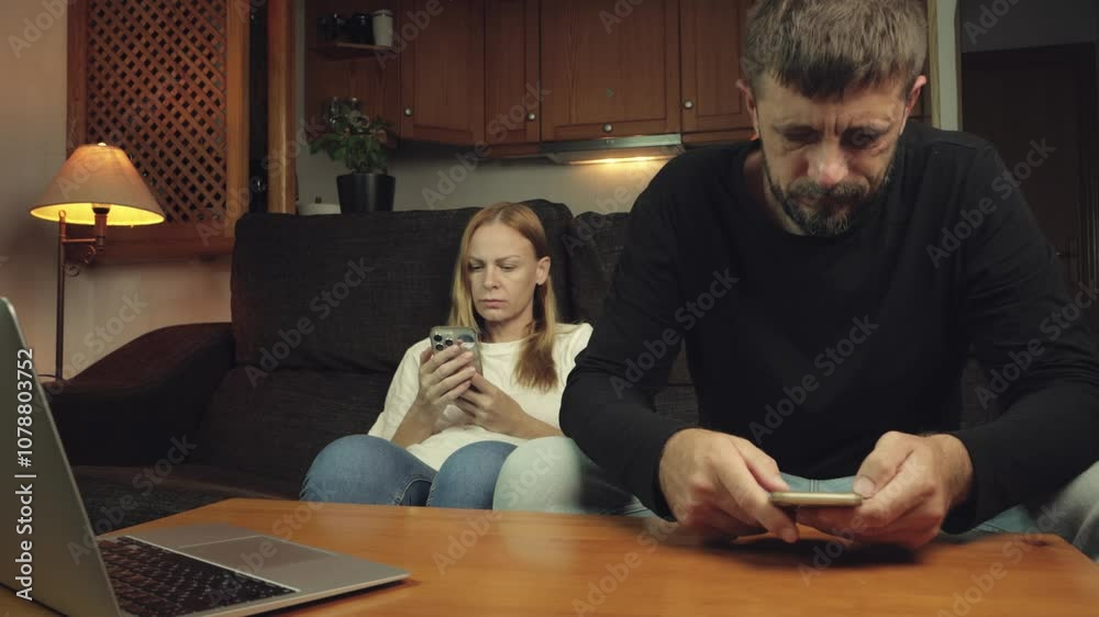 Couple sitting on  couch, absorbed in their smartphones, ignoring each other. Communication dwindles as disinterest and frustration build in their home relationship