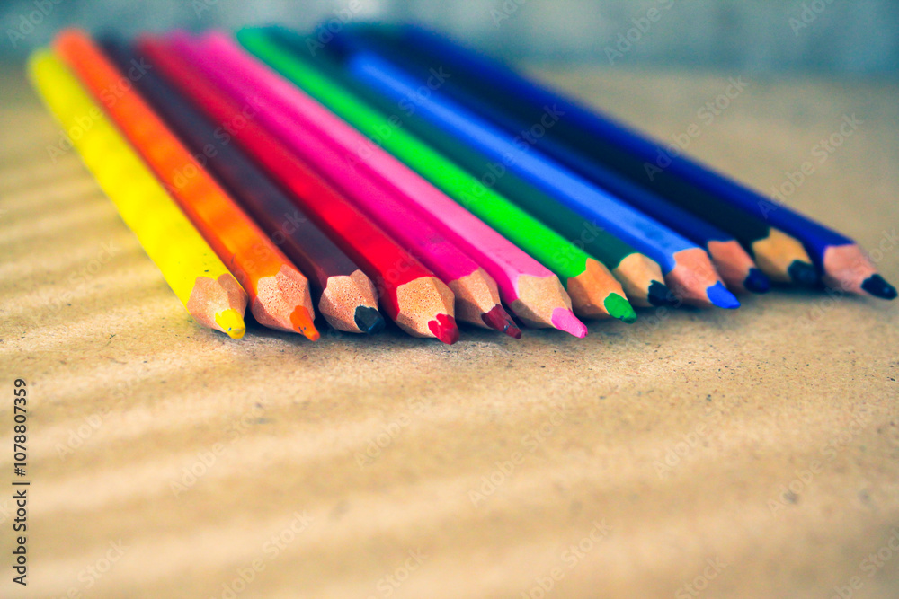 Colored pencils neatly arranged in a row, displaying a vibrant spectrum of colors on a brown surface. Perfect for themes related to art, education, and creativity. Colored pencils neatly arranged in a row, displaying a vibrant spectrum of colors on a brown surface. Perfect for themes related to art, education, and creativity.