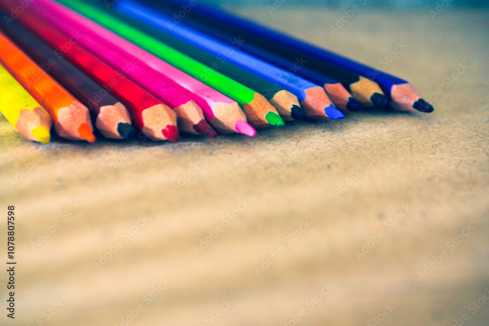 Colored pencils neatly arranged in a row, displaying a vibrant spectrum of colors on a brown surface. Perfect for themes related to art, education, and creativity. Colored pencils neatly arranged in a row, displaying a vibrant spectrum of colors on a brown surface. Perfect for themes related to art, education, and creativity.