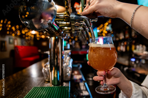 A bartender pours beer from a tap into a glass at a bar, with blurred lights and bar interior in the background. The scene captures the essence of nightlife and social gatherings photo