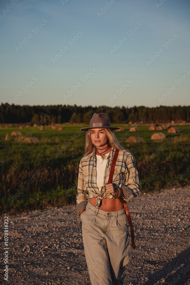 Fashionable woman walks along a gravel road in a rural setting Fashionable woman walks along a gravel road in a rural setting
