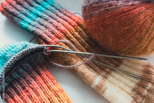 Knitted socks with rainbow gradient colours. Knitted fashion. Warm wool colourful socks. Gradient colors in clothing. Knitting hobbies. Hanicraft products. Bright knitted socks and ball of yarn. photo